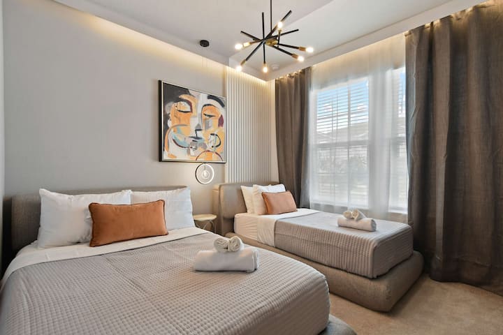 Elegantna spavaća soba s bračnim krevetima, modernom umjetnošću i toplom suvremenom atmosferom.