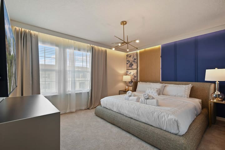 Elegantna bračna soba s odvažnim mornarskim ukrasnim zidom, modernom rasvjetom i plišanom udobnošću.