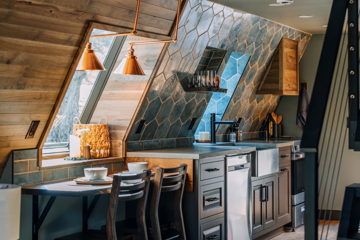 A well-equipped kitchen features modern appliances set against a backdrop of hexagon tiles in varying shades. Large windows allow natural light to illuminate the space, complemented by stylish pendant lights. A dining table with chairs provides an intimate dining option.