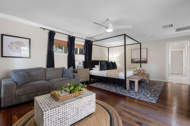 Spacious primary bedroom featuring a sleek four-poster bed, cozy sitting area, and abundant natural light.