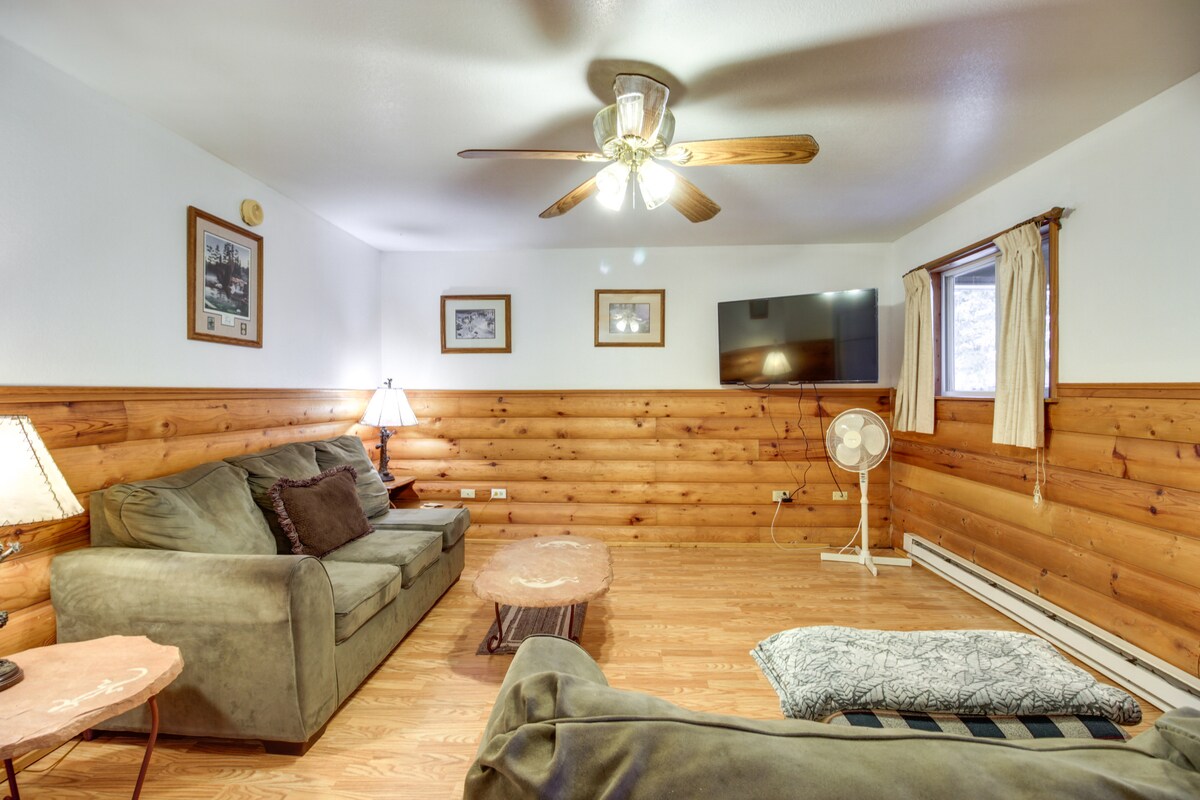 The living room showcases a wooden accent wall complemented by light-colored walls. Comfortable seating arrangements include a plush sofa and loveseat. A ceiling fan hangs above, and a TV is mounted on the wall. Natural light filters through the window, with a decorative table placed in front.