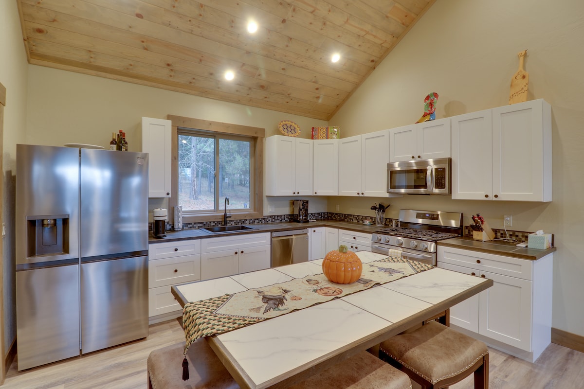 A spacious kitchen showcases modern appliances, including a stainless steel refrigerator and microwave. The white cabinetry contrasts with dark countertops. A dining table is centrally located, adorned with a decorative table runner and a pumpkin centerpiece. Natural light filters in through the window.