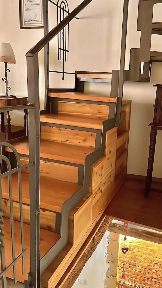 The staircase features wooden steps with built-in storage beneath each step. A sleek metal railing emphasizes the modern design, while warm wood tones create an inviting appearance. Soft lighting illuminates the area, enhancing the visual appeal.