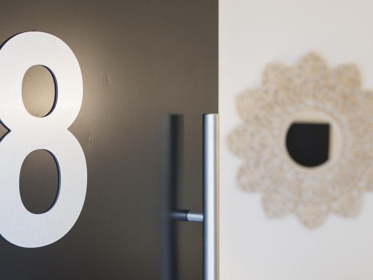 A close-up view of an apartment door featuring the number '8' in a modern silver font. Next to the door, a round mirror with a delicate, ornamental frame adds a touch of detail to the entrance area.