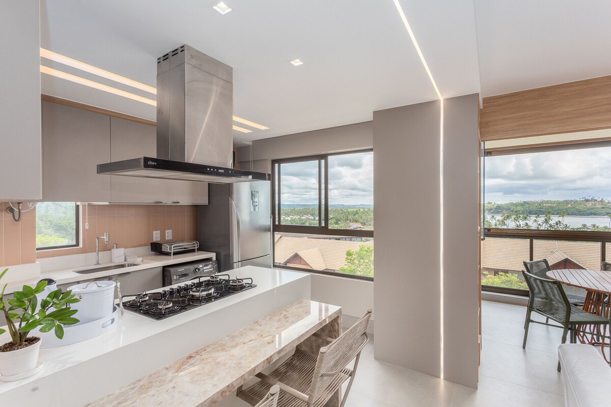 An inviting kitchen is presented with modern appliances, including an oven and a stovetop. Large windows provide ample natural light and showcase views of the surroundings. A sleek dining area with a wooden table and chairs is positioned nearby, enhancing the open layout of the space.