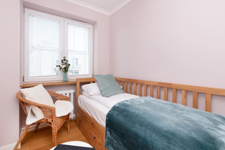 Chumba kidogo cha kulala chenye kitanda kimoja, kuta za rangi ya waridi na taa nzuri, kinachofaa kwa hali ya starehe na ya kukaribisha.