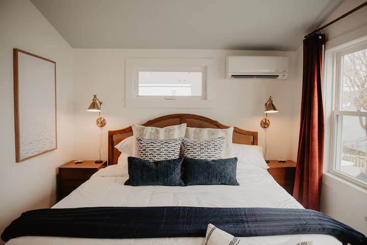Espaçoso quarto king à beira do lago com janelas grandes, uma lareira elétrica de destaque, Smart TV, armário completo e um banco aconchegante para desfrutar da vista — o conforto encontra a função neste refúgio tranquilo.