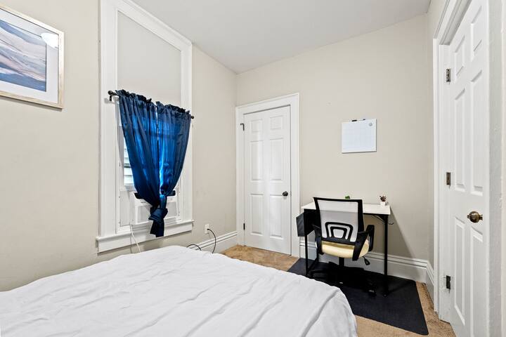 ห้องนอนที่อบอุ่นพร้อมเตียงควีนไซส์หรูหราและโต๊ะทำงานเหมาะสำหรับการทำงานหรือพักผ่อน
