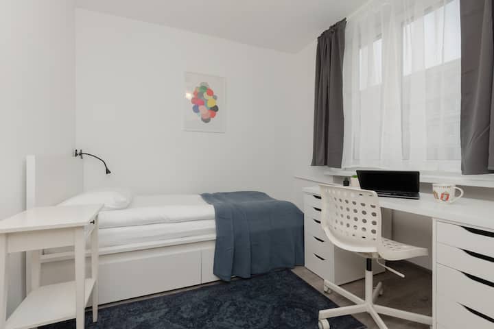 ห้องนอนมีสไตล์พร้อมเตียงสีขาวเครื่องนอนสีฟ้าโต๊ะทำงานและงานศิลปะกรอบรูปบนผนัง