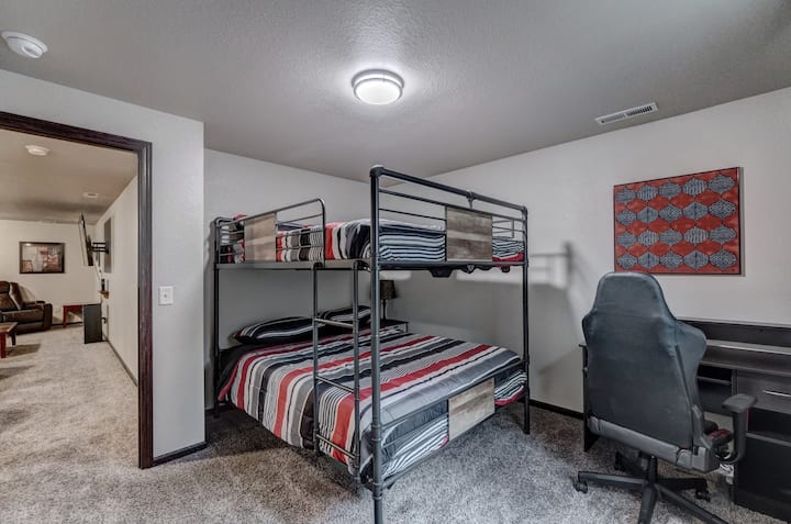 חדר שינה בקומה התחתונה (3) עם מיטת קומתיים קווין מעל קווין, שידת לילה עם מטעני USB מובנים, שולחן גדול וכיסא משחקים ארגונומי.