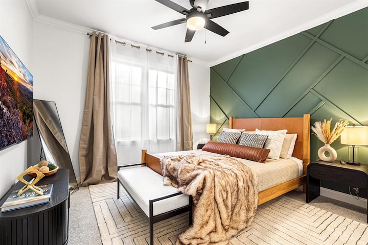 Camera per gli ospiti al piano principale con letto queen-size, Smart TV da 55" e una parete verde con motivi geometrici. Condivide un bagno comunicante con la camera da letto adiacente.