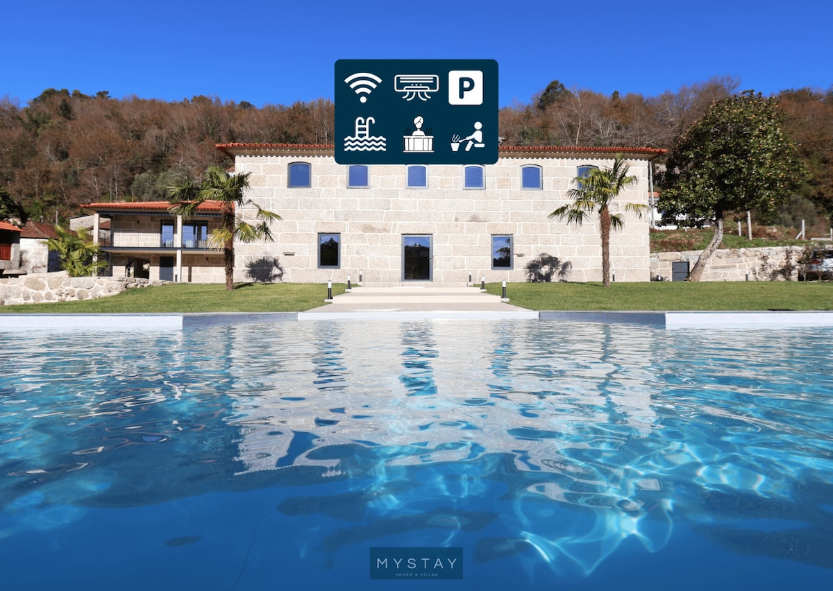 A clear blue swimming pool reflects the bright sky and is framed by manicured grass and palm trees. The elegant stone structure with arched windows stands prominently in the background, providing an inviting view of the shared outdoor amenities.