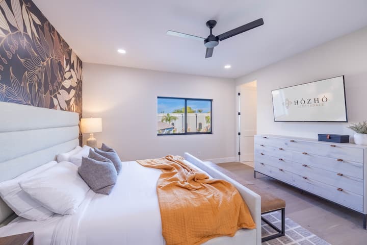 King Bedroom 5 w/Ensuite: Mapumziko ya kisasa ya wageni yenye ukuta wa kifahari, mwonekano wa bwawa, matandiko ya plush na televisheni ya skrini bapa.
