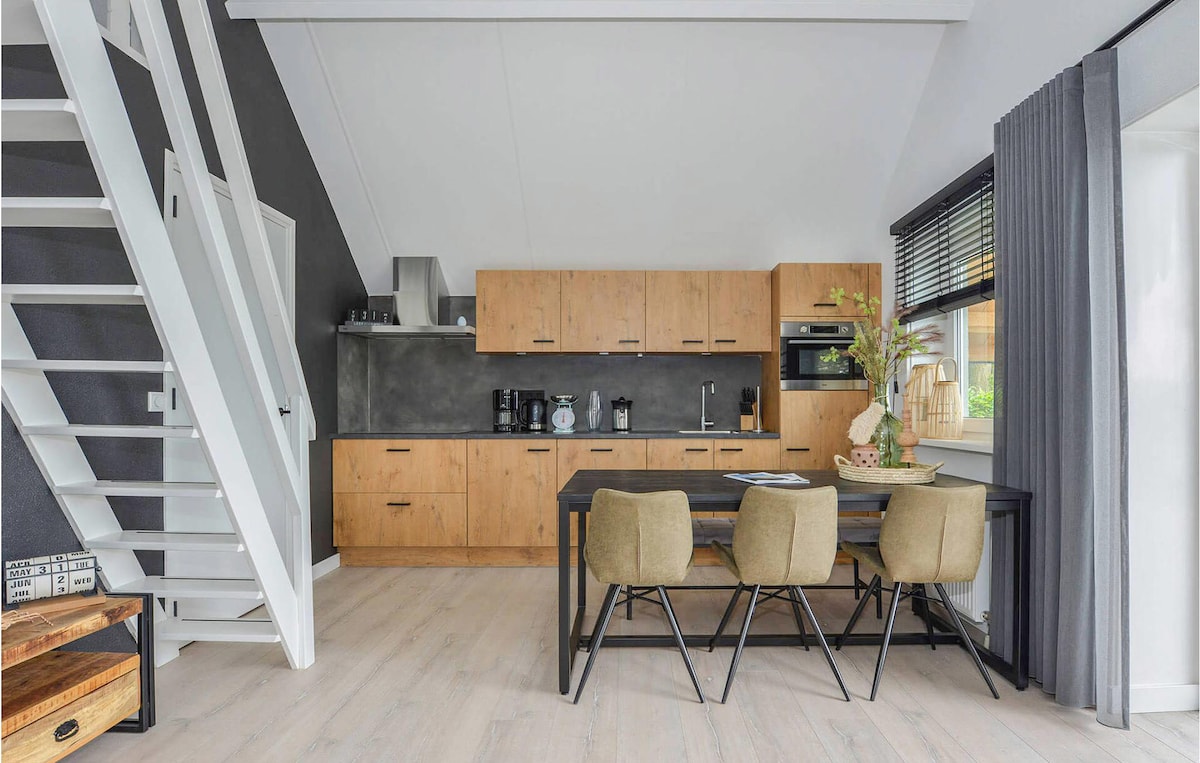 A modern kitchen area with light wood cabinetry and dark counter surfaces is showcased. The dining table with four chairs is positioned nearby, accentuated by natural light from the windows. A staircase leads to the upper floor, adding to the spacious feel of the room.