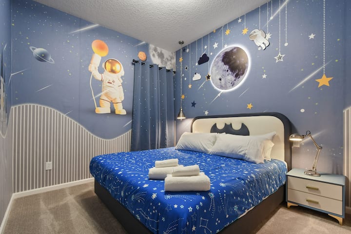 Dormitorio con temática espacial con una decoración brillante de la luna, murales de astronautas y una acogedora cama estrellada.