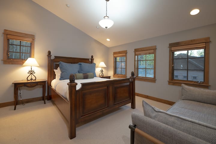 Sink into plush comfort in your spacious bedroom, where warm wood tones and soft blue accents create a peaceful retreat. Natural light flows through multiple windows as you unwind on the cozy seating area.
