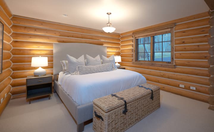 Drift off to sleep surrounded by warm log cabin walls and crisp white linens. Your cozy retreat features a plush king bed and peaceful forest views through the window, creating the perfect mountain escape.