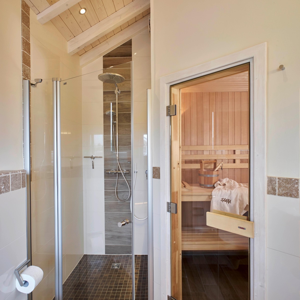 A modern bathroom is showcased, featuring a glass shower with a rainfall showerhead and a stylish sauna in the background. Natural wood accents are present on the sauna's interior, and a soft towel is neatly placed inside, enhancing the serene atmosphere.