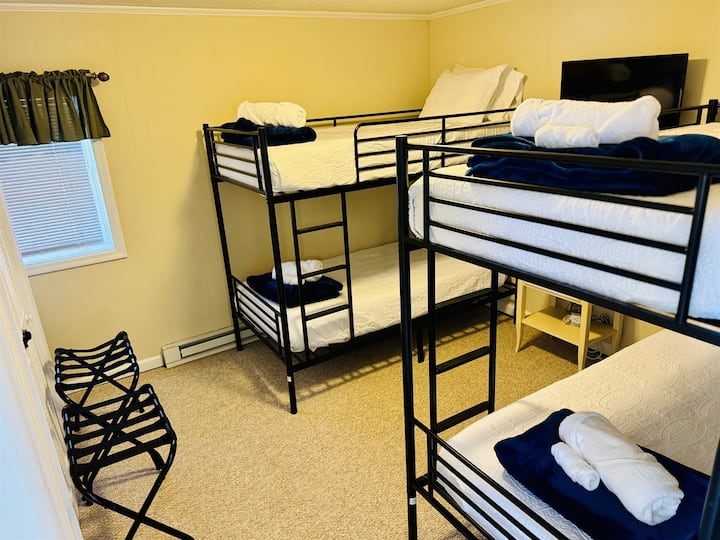 Lower Level Bunk Room beside the game room features 4 Twin beds, a nightstand, charging outlets with USB ports, 4 luggage racks, a closet to hang clothes, & a Roku Smart TV.