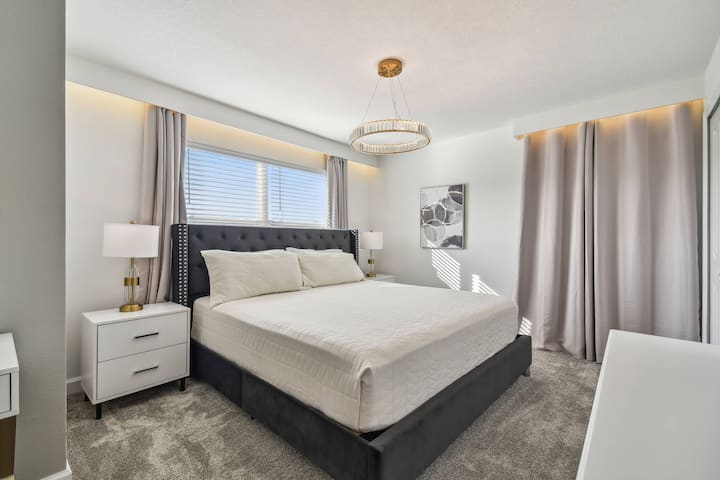 Vstúpte do svetlej, vzdušnej spálne zdobenej mäkkým sivým kobercom a jemnými neutrálnymi tónmi. Šik posteľ, orámovaná štýlovými lampami a elegantnými závesmi, láká k relaxácii, zatiaľ čo veľké okno zapĺňa miestnosť prirodzeným svetlom.