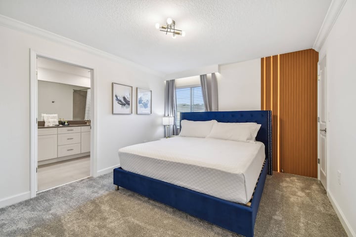 Vstúpte do útulnej spálne s mäkkým rámom postele v námorníckej modrej farbe doplneným mäkkým sivým kobercom. Prirodzené svetlo prúdi cez veľké okno a umocňuje pokojnú atmosféru, zatiaľ čo moderné umelecké diela dodávajú priestoru osobnosť.