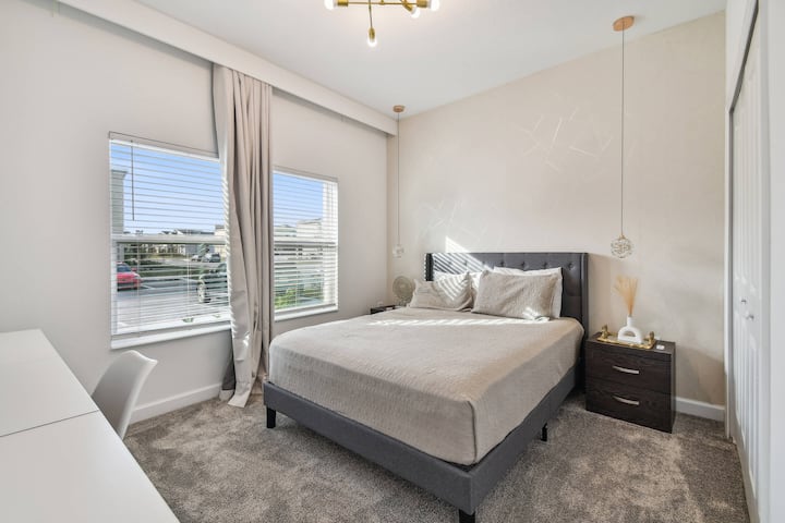 Vychutnajte si bohaté prírodné svetlo v tejto útulnej spálni s mäkkou sivou posteľou a jemnými neutrálnymi tónmi pre upokojujúcu atmosféru. Minimalistický dekor a elegantný nočný stolík zvýrazňujú vaše pohodlie počas pobytu.