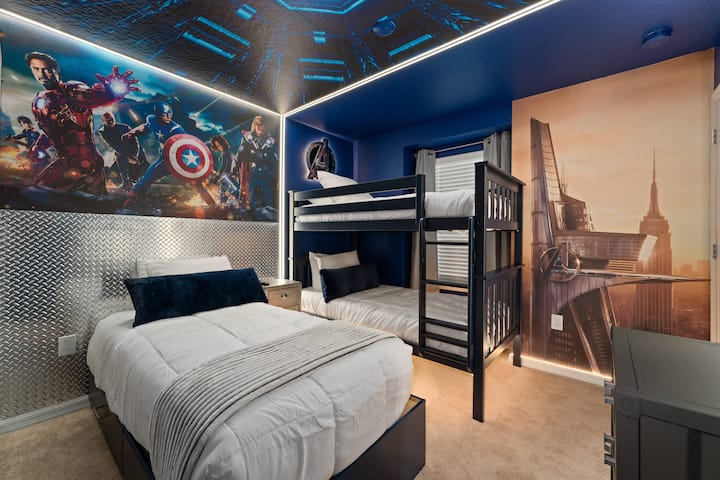 Vitajte v živej detskej spálni s hravými nástennými maľbami superhrdinov, ktoré podnecujú predstavivosť. Útulná biela posteľná bielizeň sa dokonale hodí k odvážnym modrým stenám a kovovým detailom a vytvára zábavné a pohodlné útočisko pre vaše deti.
