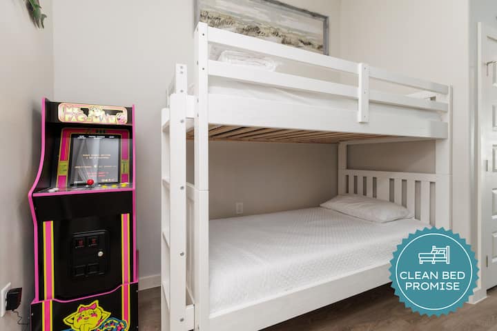 Tu divertido dormitorio cuenta con literas de un blanco inmaculado y una máquina recreativa vintage para que te diviertas sin fin.