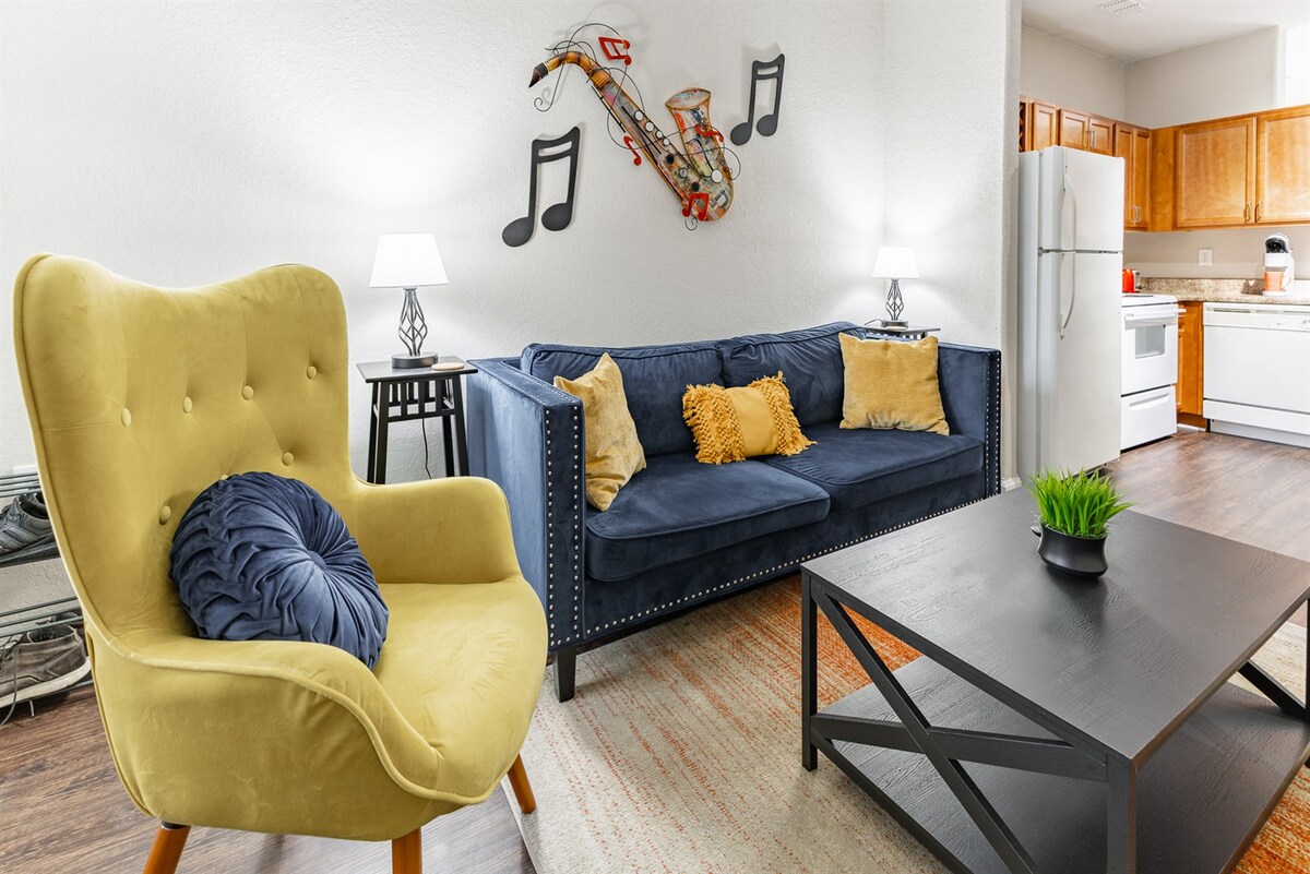 The living area features a blue sofa adorned with yellow and navy pillows, paired with a stylish green armchair. A coffee table sits in the center, while wall art depicting musical notes and a saxophone enhances the ambiance. Soft lighting from lamps creates a cozy atmosphere.