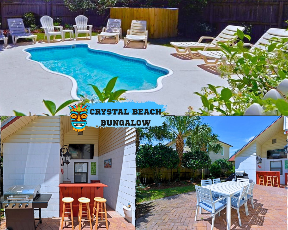 A private splash pool is surrounded by loungers and greenery. A poolside bar with an outdoor TV and grill is visible, offering a casual dining area. The spacious patio features a large table, ideal for gatherings, with palm trees adding a tropical feel.