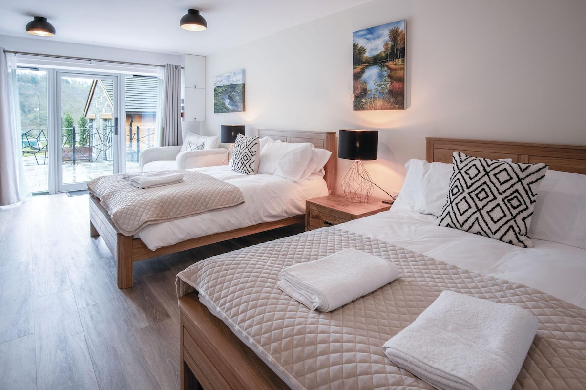 The spacious twin suite features two comfortable double beds, adorned with neutral bedding and decorative pillows. A cozy seating area is visible, along with a view of the outdoors through large glass doors that lead to a private courtyard.