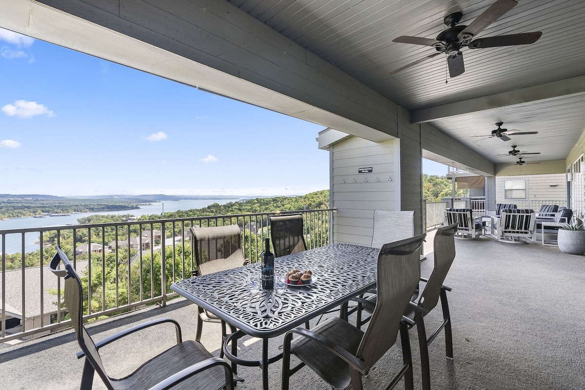 A spacious deck features a large dining table with comfortable chairs, set against a backdrop of Table Rock Lake's stunning views. The area is complemented by ceiling fans, enhancing the inviting atmosphere for gatherings in the fresh air.