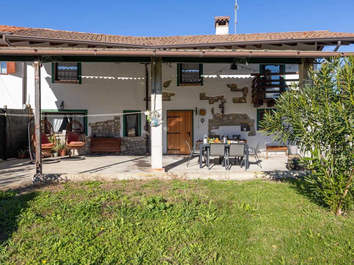 The exterior of the terraced house features a covered terrace with seating for dining. A lush green garden surrounds the space, while unique stone accents complement the building's facade. Two hanging chairs add a cozy touch, inviting relaxation in an outdoor setting.