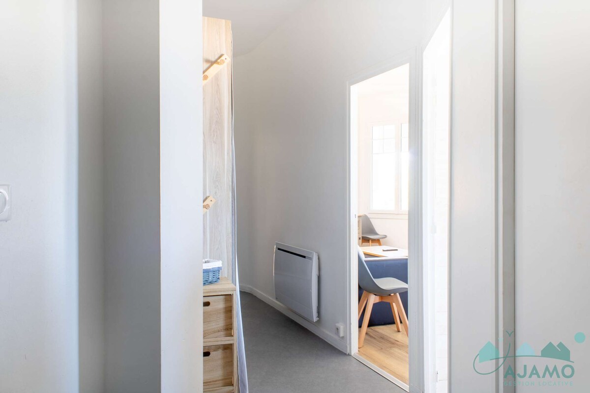 A bright and minimalist hallway features a light colour scheme, enhancing the sense of space. There are wooden storage units and wall hooks for coats. A view into the living area is provided, with ample natural light flowing through an adjacent door.