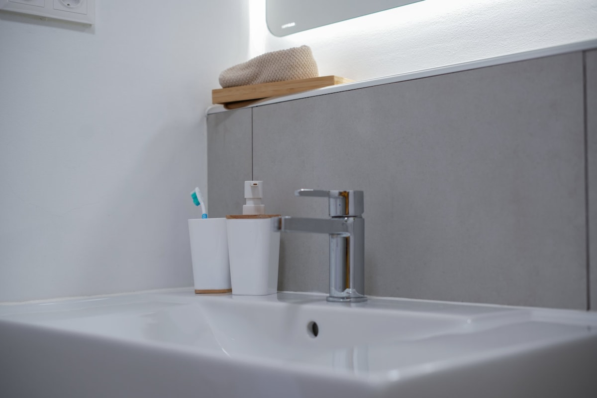 A modern bathroom sink is featured, showcasing a sleek chrome faucet above a smooth white basin. Personal care items are neatly arranged, including a toothbrush and a soap dispenser in minimalist containers, emphasizing a clean and organized space.