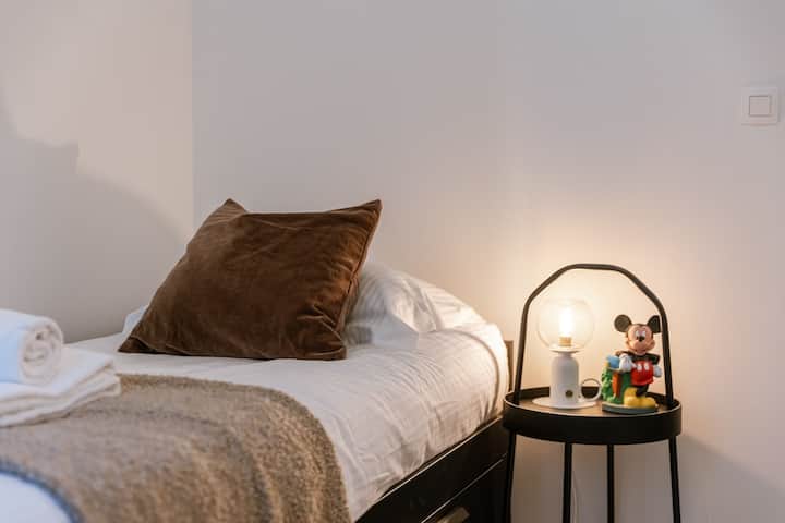 Pohodlná jednolôžková posteľ s teplým osvetlením pri nočnom stolíku.