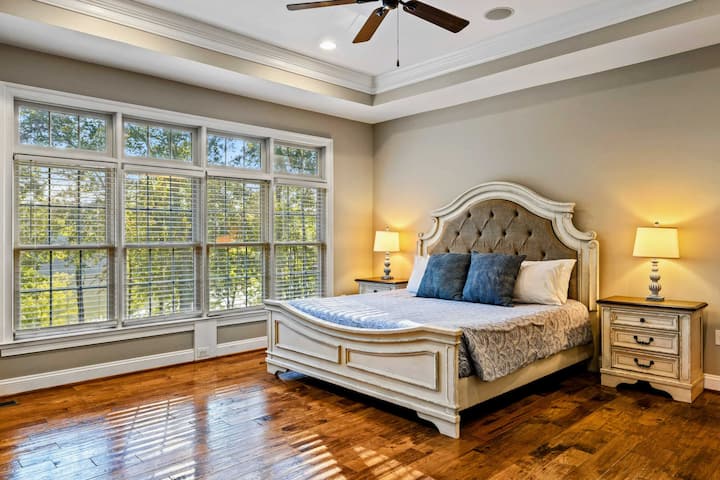 Habitación con baño 2 - Una cama king con cabecera acolchada, techo con molduras y grandes ventanales con vista a los árboles.