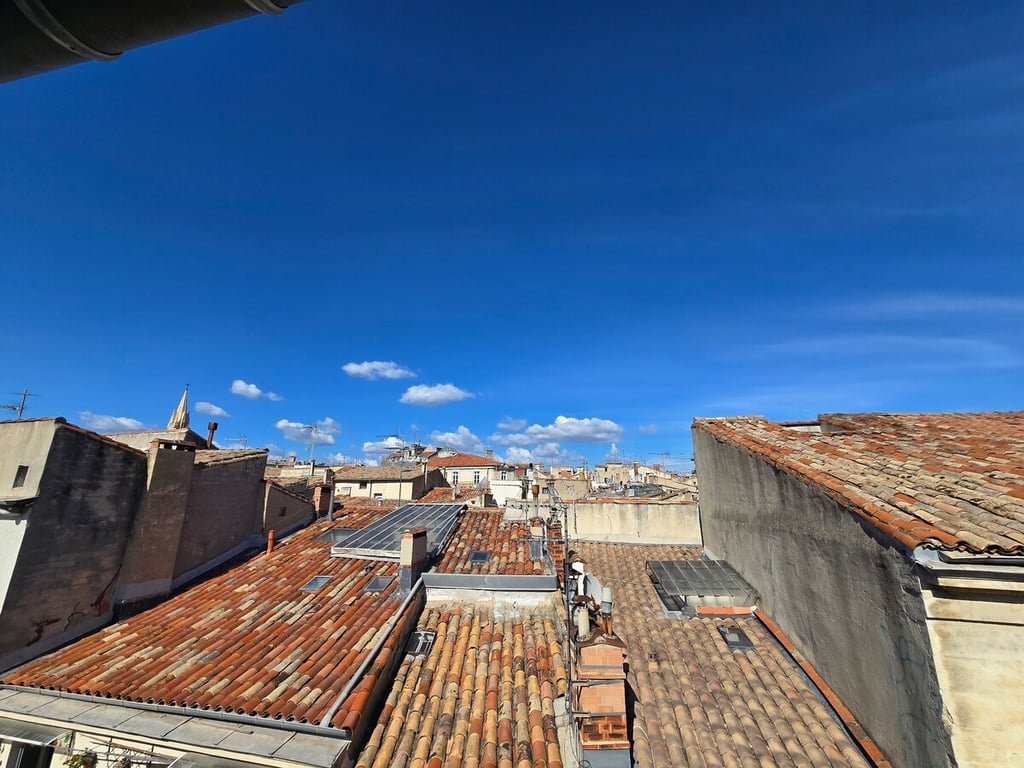 A panoramic view reveals terracotta rooftops of nearby buildings under a clear blue sky. Soft white clouds drift peacefully above the historical architecture, showcasing the charm of the local area. The image captures the essence of the surrounding environment from the studio's vantage point.