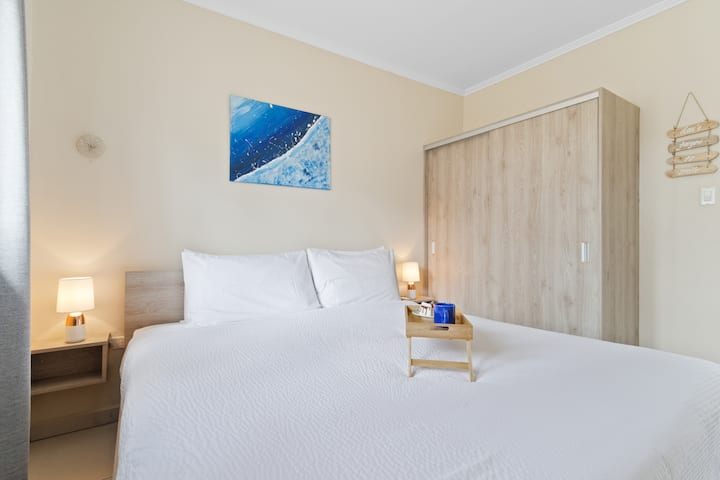 Dormitorio exclusivo del apartamento en Noord, Aruba - Cómoda cama tamaño king - Habitación elegantemente decorada con grandes pinturas murales estéticas - Lámparas de mesa majestuosas - Ropa de cama ordenada y limpia con almohadas suaves - Espejo de pie de tamaño grande