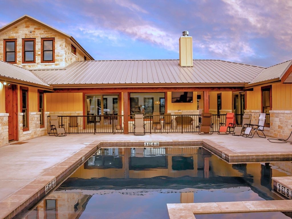 An inviting outdoor area features a private pool reflecting the sky, complemented by a sun-soaked patio with several loungers. The space is bordered by a stylish building with large windows, allowing for views of the interior. Tranquil evening colors enhance the serene atmosphere.
