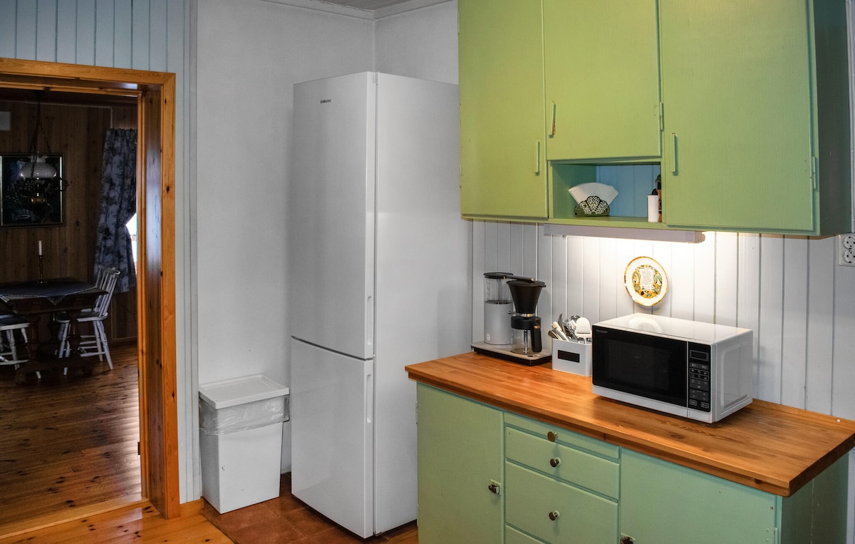 A compact kitchen features light green cabinetry and wooden countertops. Major appliances include a white refrigerator, a microwave, and a coffee maker. A trash bin is positioned near the fridge, while natural light brightens the space, adding warmth to the interior.