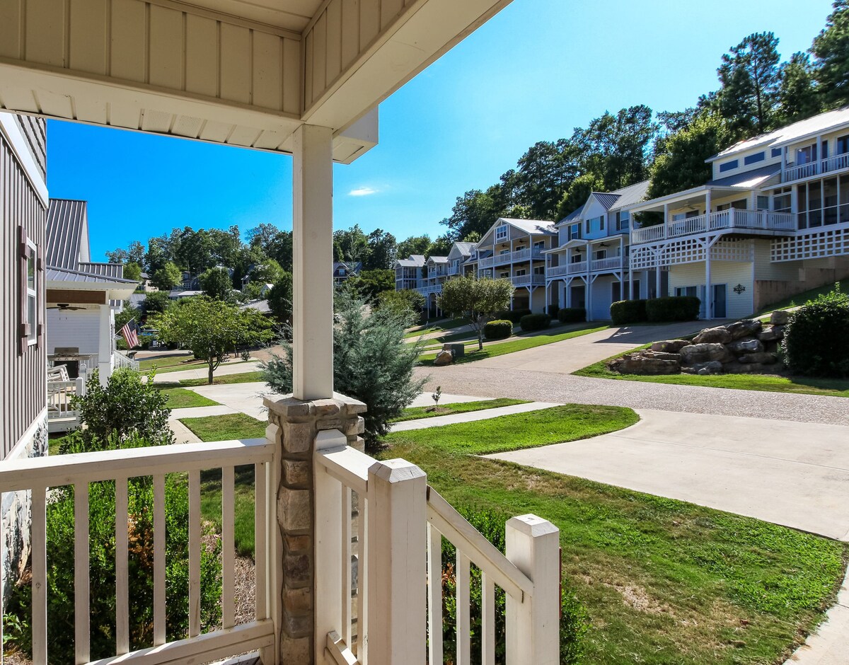 A view from the porch captures a landscaped neighborhood with well-maintained homes. The roadway is lined with grass and trees, providing a quiet and inviting atmosphere. Sidewalks and driveways are visible, leading to the nearby houses, creating a sense of community.