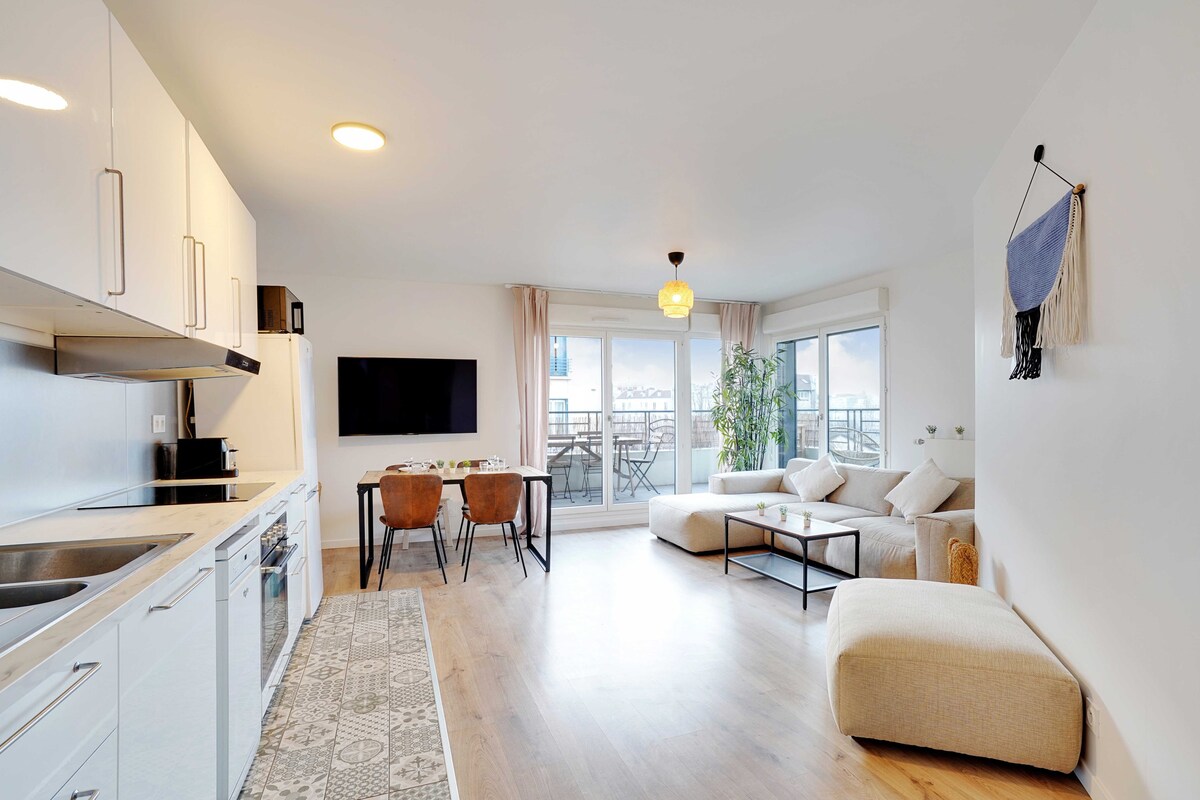 An open-concept living area features a modern kitchen with sleek cabinetry and appliances, a spacious sofa for relaxation, and a dining table surrounded by four chairs. Large glass doors lead to a private balcony, enhancing the natural light in the room.