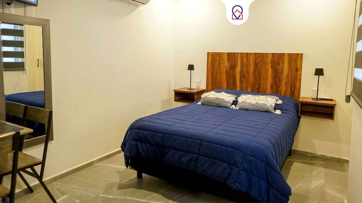 A spacious sleeping area is equipped with a large bed featuring a wooden headboard. Two bedside tables with lamps are placed on either side. A mirror and a small table are positioned nearby, adding functionality to the room's layout.
