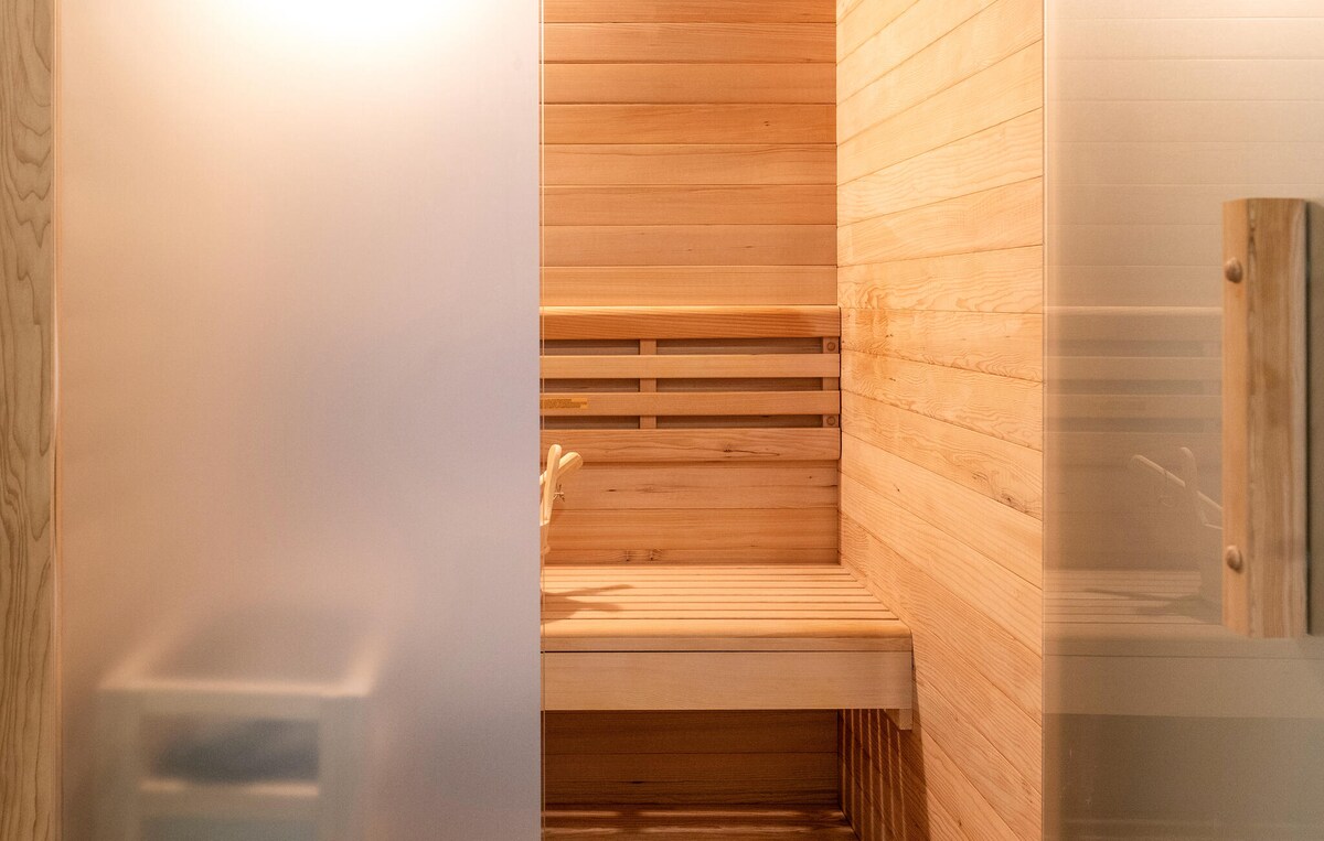 The sauna features warm wooden paneling and a minimalist design. Smooth benches provide seating, while frosted glass doors add a touch of privacy. Soft light diffuses through the glass, creating a serene atmosphere ideal for relaxation.