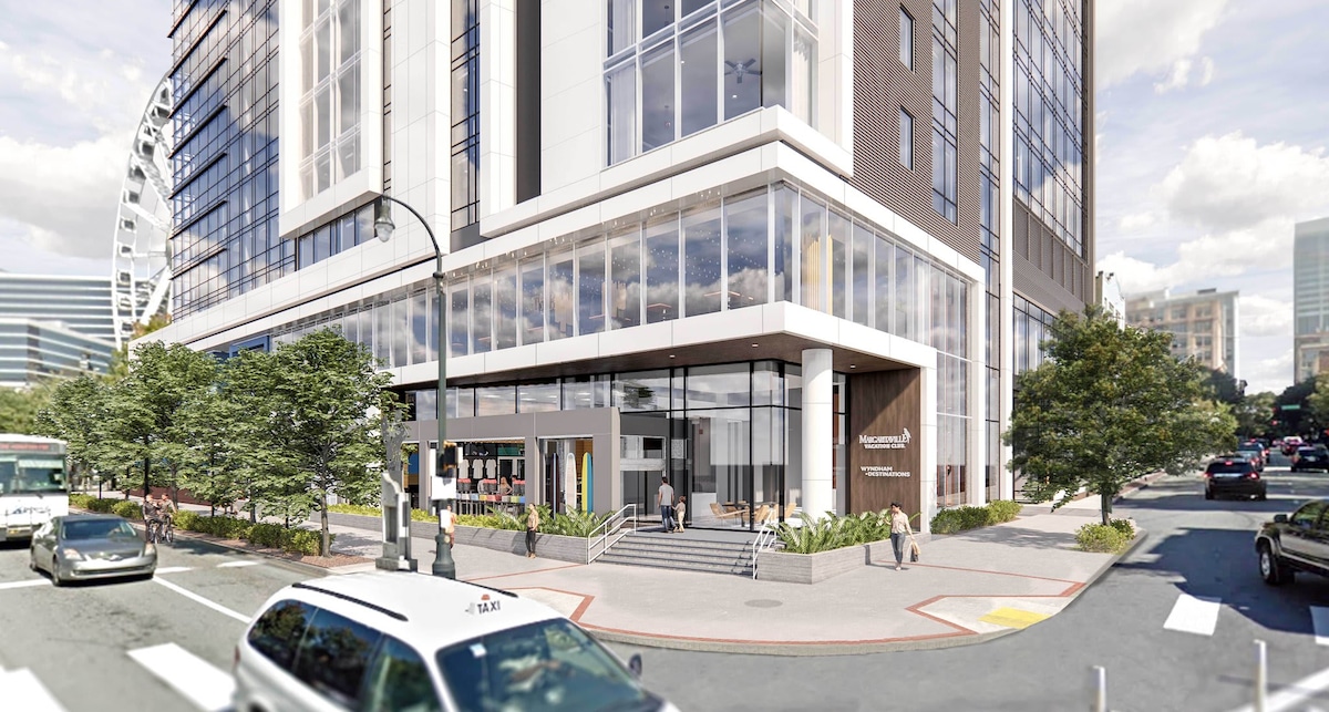 A modern building with a glass facade is featured at street level, showcasing an inviting entrance. The area includes well-maintained landscaping with trees and shrubs, while pedestrians and vehicles populate the busy urban street.