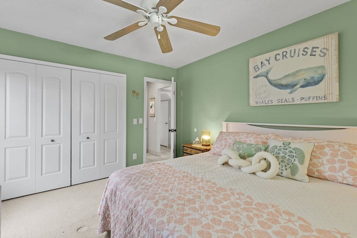 Საძინებელში არის რბილი მწვანე კედლები, კომფორტული საწოლი პასტელური თეთრეულით და მომხიბლავი სანაპირო დეკორი. Ჭერის ვენტილატორი და საკმარისი კარადა აუმჯობესებს ოთახის პრაქტიკულობას, რაც იდეალურია დასვენებისთვის.