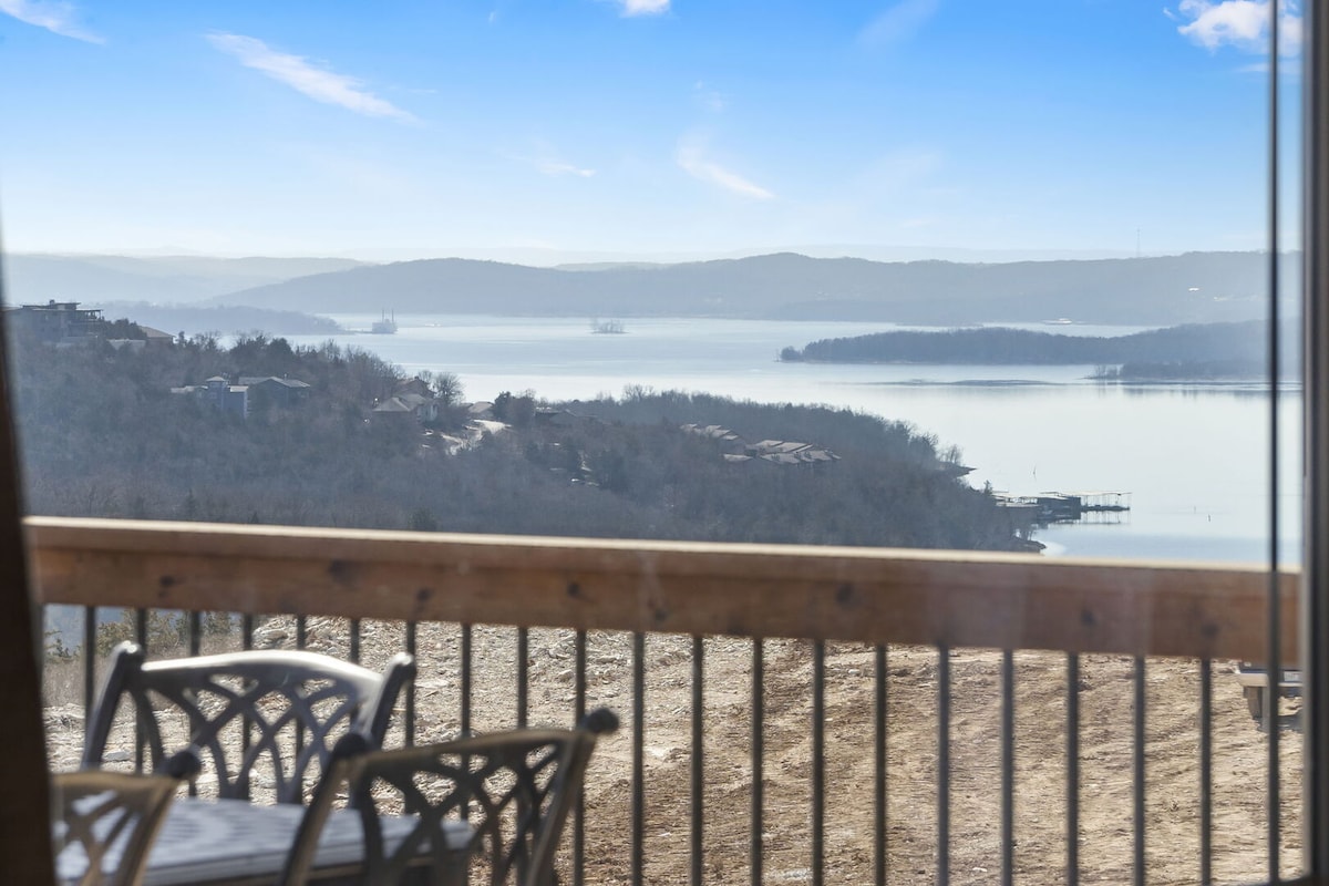 A scenic view of the tranquil lake and surrounding hills is captured from the upper deck of the lodge. The serene water reflects the sky, while distant hills provide a natural backdrop, creating an inviting setting for outdoor relaxation.