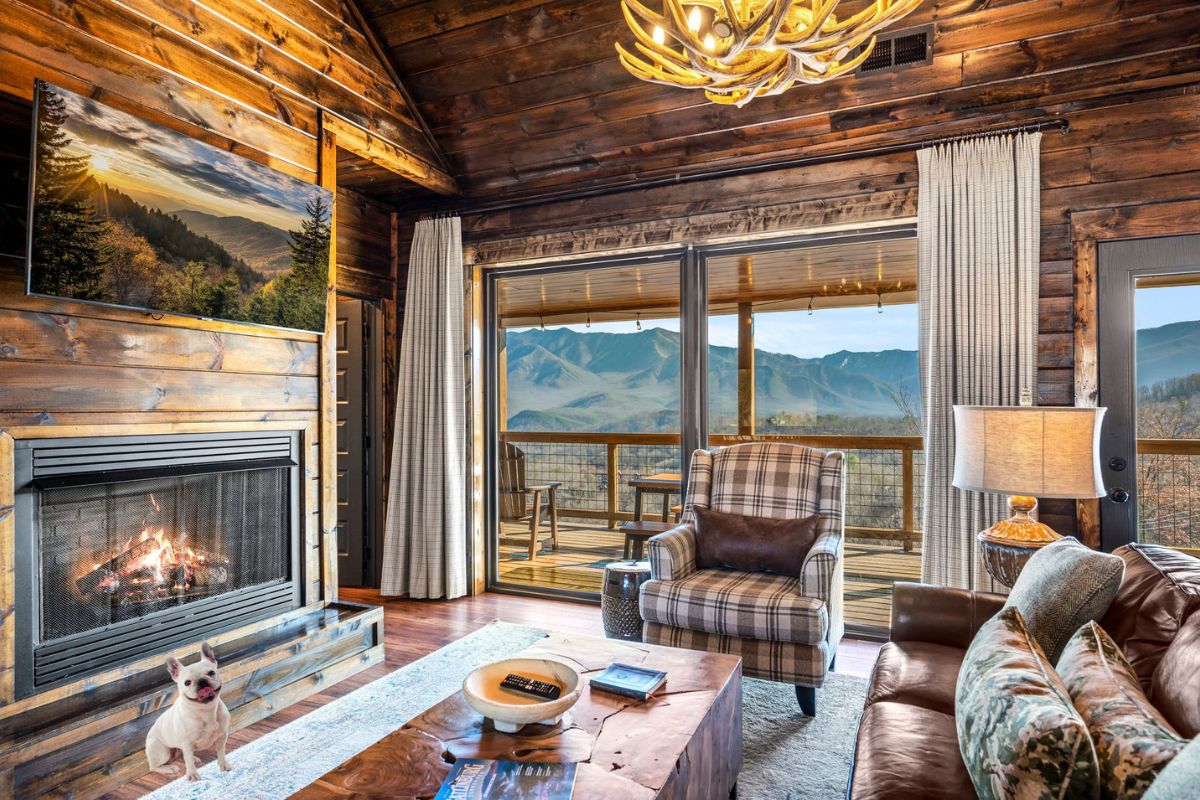 A warm living area features a gas fireplace as a focal point, complemented by a large window offering expansive views of the mountains. Comfortable seating includes a leather sofa and an armchair, while decorative accents enhance the inviting atmosphere.