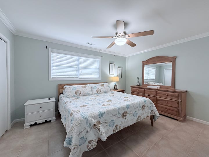 غرفة نوم مشرقة بسرير كينج مع ديكور ساحلي وخزانة ملابس كبيرة ومروحة سقف.